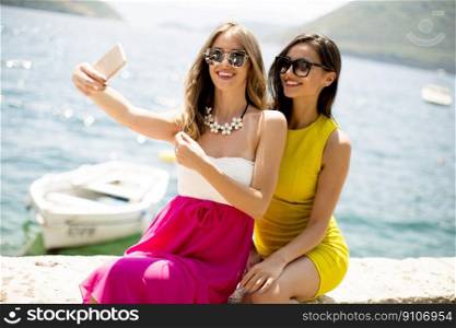 Two pretty young women taking selfie with mobile phone by the sea