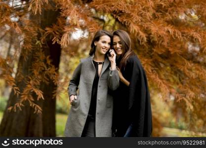 Two pretty young women using mobi≤pho≠in the autumn park