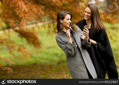 Two pretty young women using mobile phone in the autumn forest