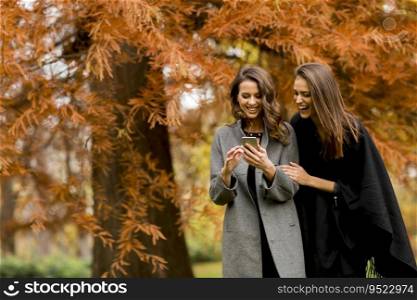 Two pretty young women using mobile phone in the autumn park
