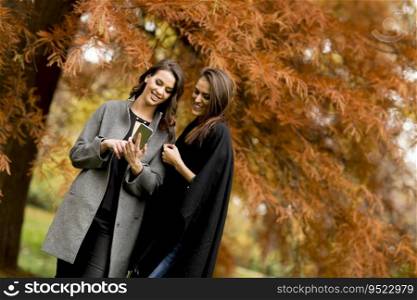 Two pretty young women using mobile phone in the autumn park