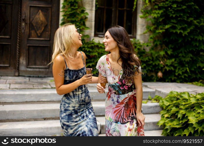 Two pretty young women walking and eating ice cream by the old house with ivy