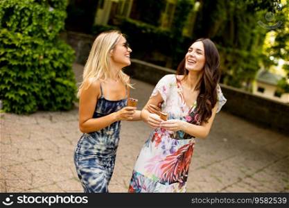 Two pretty young women walking and eating ice cream by the old house with ivy