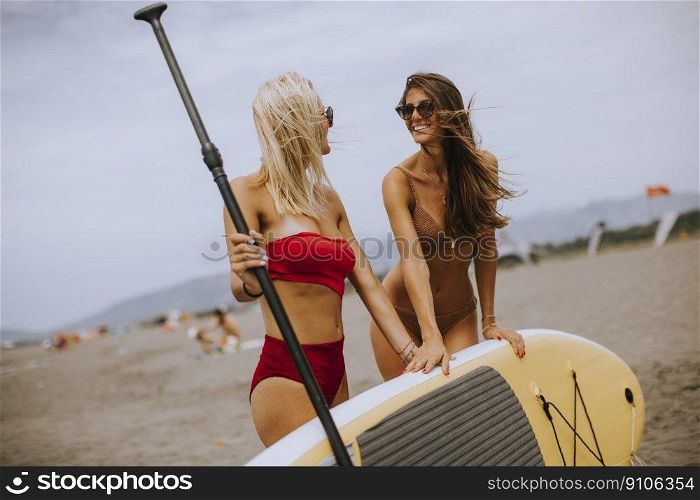 Two pretty young women with paddle board on the beach on a summer day
