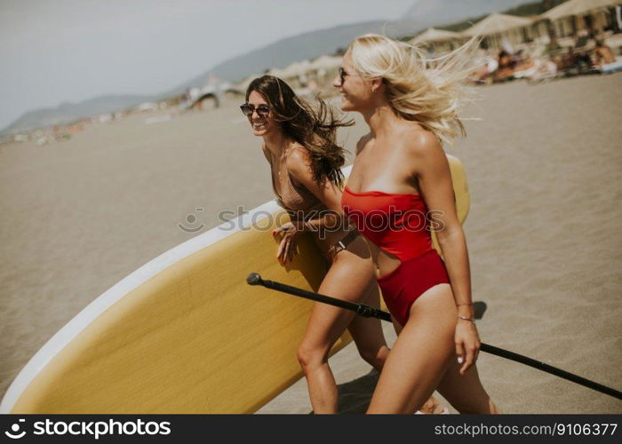 Two pretty young women with paddle board on the beach on a summer day