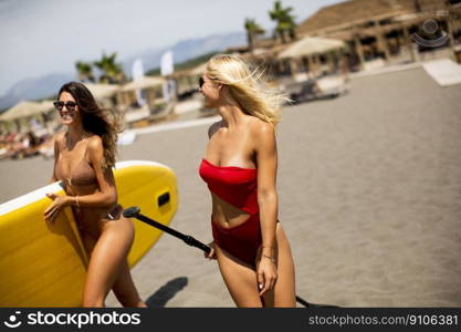 Two pretty young women with paddle board on the beach on a summer day