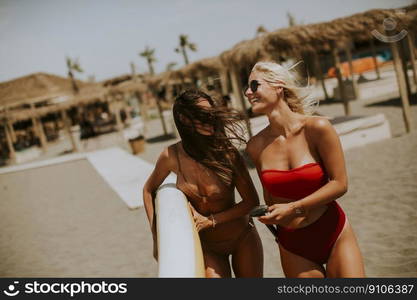 Two pretty young women with paddle board on the beach on a summer day