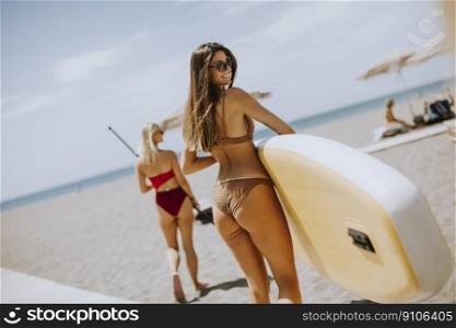 Two pretty young women with paddle board on the beach on a summer day