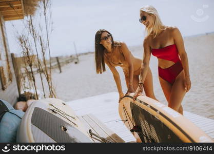 Two pretty young women with paddle board on the beach on a summer day