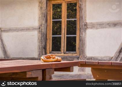 Two pretzels, a specific German pastry product, on a wooden table, in front of an old rustic house, with German traditional features.