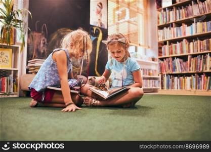 Two primary schoolgirls doing homework in school library. Students learning from books. Pupils having fun in library. Back to school