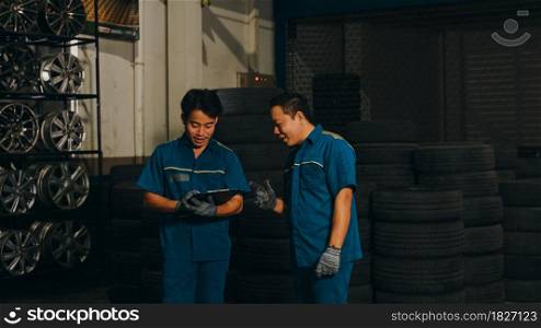 Two professional car mechanic using paperwork makes the oil and engine check to the car on lifted automobile at repair service station at night. Skillful Asian guy in uniform fixing car. Car service.