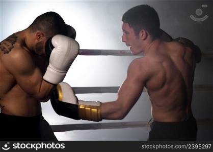 Two professional young muscular shirtless male boxers fighting in a boxing ring. High quality photography.. Two professional young muscular shirtless male boxers fighting in a boxing ring.