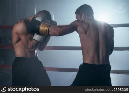 Two professional young muscular shirtless male boxers fighting in a boxing ring. High quality photography.. Two professional young muscular shirtless male boxers fighting in a boxing ring.