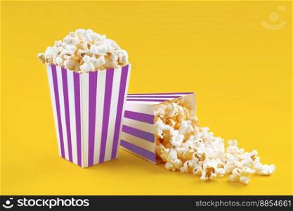 Two purple white striped carton buckets with tasty cheese popcorn, isolated on yellow background. Box with scattering of popcorn grains. Movies, cinema and entertainment concept.