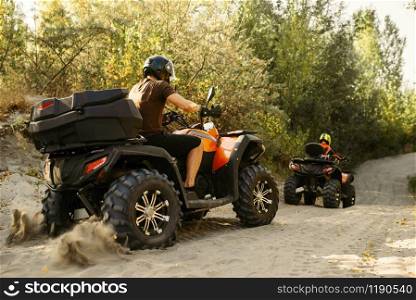 Two quad bike riders in helmets travels in forest, front view. Riding on atv, extreme sport and travelling, quadbike adventure. Two quad bike riders travels in forest, front view