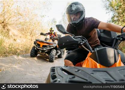 Two quad bike riders in helmets travels in forest, front view. Riding on atv, extreme sport and travelling, quadbike adventure. Two quad bike riders travels in forest, front view