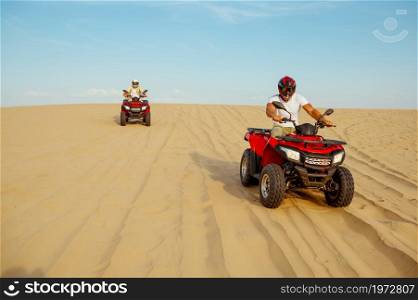 Two racers coming down from the dunes on atv, desert sands. Male persons on quad bikes, sandy race, safari in hot sunny day, 4x4 extreme adventure, quad-biking. Two racers coming down from the dunes on atv