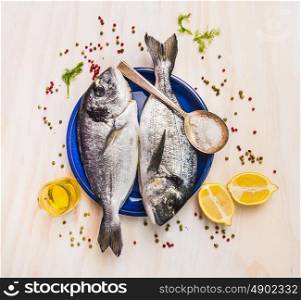 two raw dorado fish in blue plate with spoon,lemon,herb and spices, top view