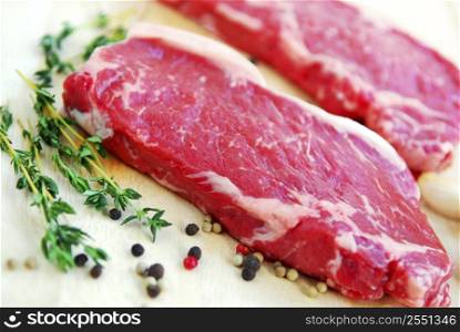 Two raw new york steaks on cutting board with thyme and peppercorns