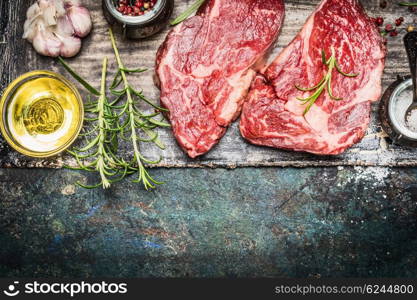 Two raw steaks with oil and spices on dark rustic background, top view, border