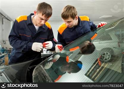 Two Real Mechanics changing the broken windshield of black car in Auto Repair Shop