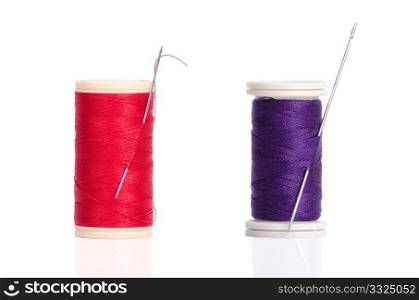 Two red and purple thread bobbin and needle isolated on white background.