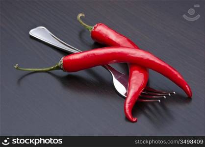 Two red chili peppers and fork on the kitchen table
