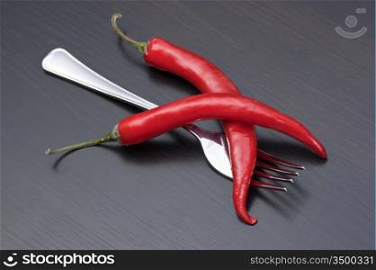 Two red chili peppers and fork on the kitchen table