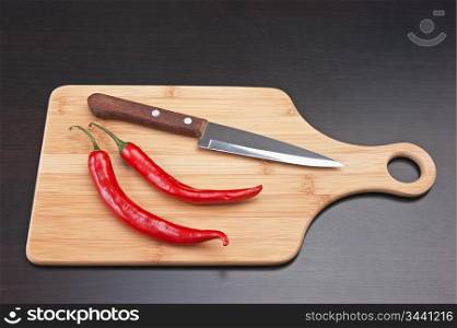 Two red chili peppers and knife on the kitchen table