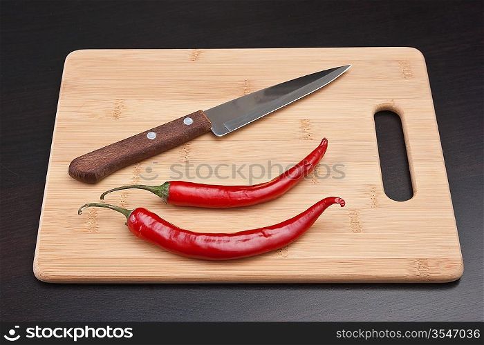 Two red chili peppers and knife on the kitchen table