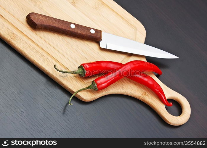 Two red chili peppers and knife on the kitchen table