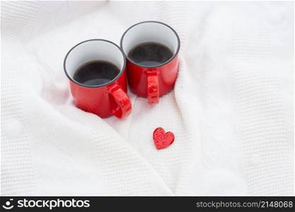Two red cups of coffee together with a small red heart, coffee in bed. Surprise, valentine&rsquo;s day celebration concept. Two red cups of coffee together with a small red heart, coffee in bed. Surprise, valentine&rsquo;s day celebration concept.