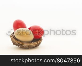 Two red eggs and one gold egg in nest reflect important choices in business and investing. Copy space on white background.