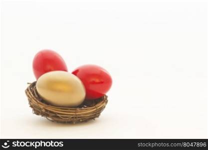 Two red eggs and one gold egg in nest reflect important choices in business and investing. Copy space on white background.