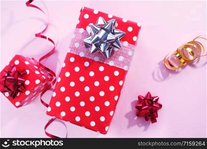 Two red gift boxes in white polka dots and a silver and red bow, red and gold serpentine, red bow on a pink background.
