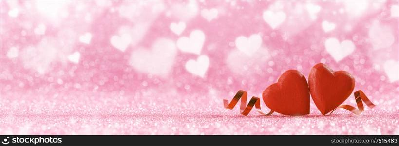 Two red handmade wooden hearts and ribbons on pink bright glitter lights bokeh background. Two hearts and ribbons