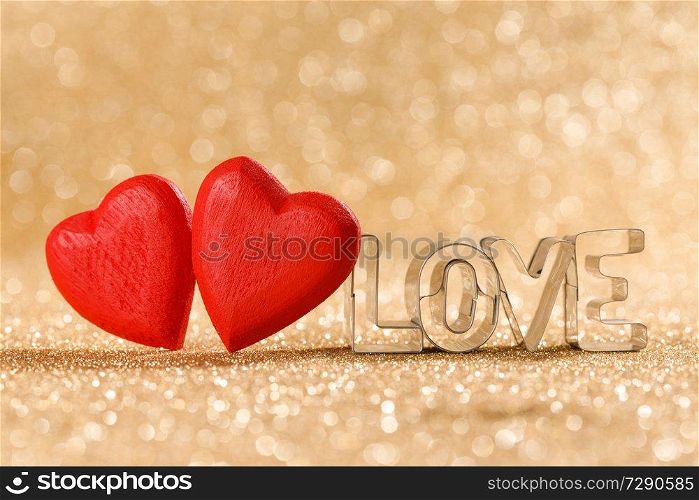 Two red handmade wooden hearts and word love on golden bright glitter lights bokeh background. Red hearts on glitter background