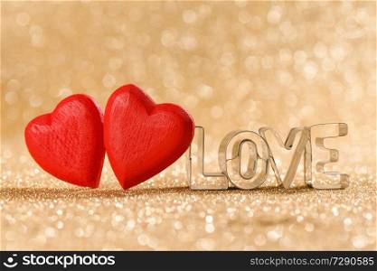 Two red handmade wooden hearts and word love on golden bright glitter lights bokeh background. Red hearts on glitter background