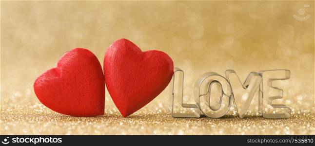 Two red handmade wooden hearts and word love on golden bright glitter lights bokeh background. Wooden hearts and word love