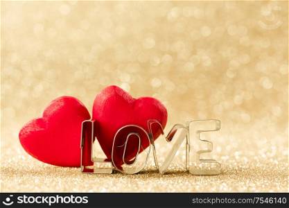 Two red handmade wooden hearts and word love on golden bright glitter lights bokeh background. Wooden hearts and word love