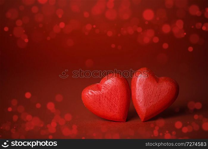 Two red handmade wooden hearts on red lights bokeh background. Red hearts on glitter background