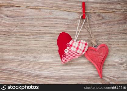 two red  hearts hanging together on rope on wooden background
