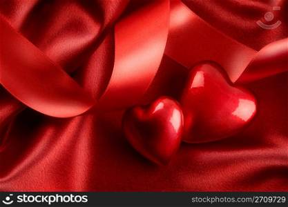 Two red hearts with ribbon on satin