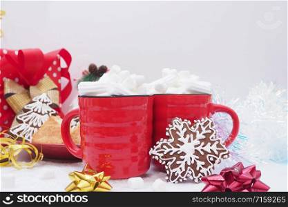 Two red mugs with coffee and marshmallows, gingerbread cookies with icing in the form of snowflakes and Christmas trees, ribbons, tinsel, bows on a white background.