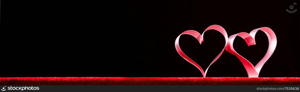 Two red ribbon hearts on black background with copy space for text, Valentines day concept. Red ribbon hearts on black