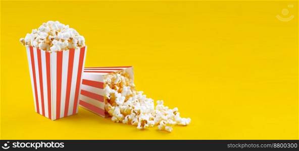 Two red white striped carton buckets with tasty cheese popcorn, isolated on yellow background. Box with scattering of popcorn grains. Movies, cinema and entertainment concept.