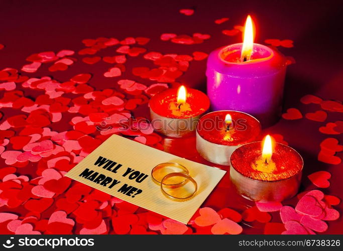 Two rings and a card with marriage proposal with four candles on the red background