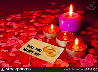 Two rings and a card with marriage proposal with four candles on the red background