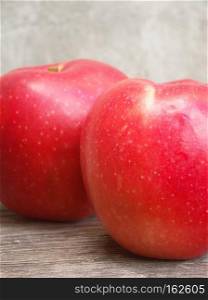 Two ripe red apples on wooden table against concrete wall.